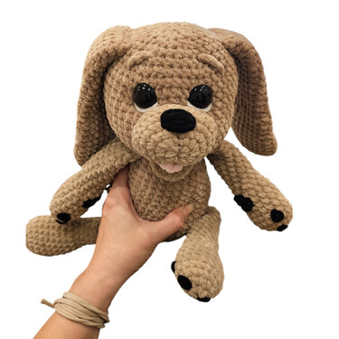 Beiger Amigurumi-Hund aus Chenillegarn mit Schlappohren, in einer Hand gehalten