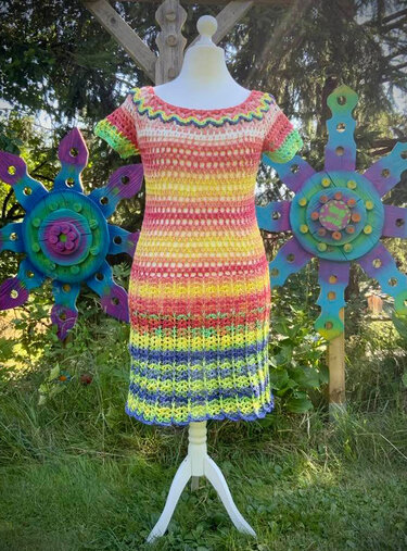 Gestreiftes, farbenfrohes Häkelkleid mit kurzen Ärmeln auf einer weißen Schaufensterpuppe im Garten.