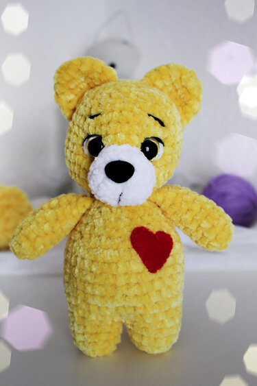 Yellow crocheted amigurumi teddy bear with a red heart on its chest and a white snout.
