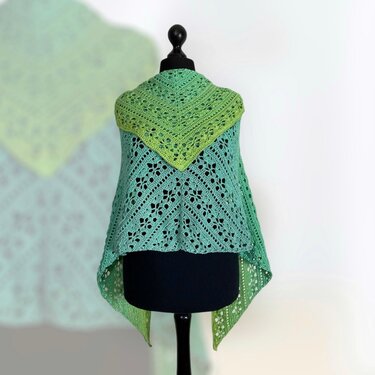 Triangle crochet shawl in green-to-teal gradient with floral lace motifs draped on a black dress form