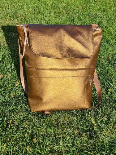 Rucksack in goldfarbener Optik mit Reißverschlussfach auf Gras