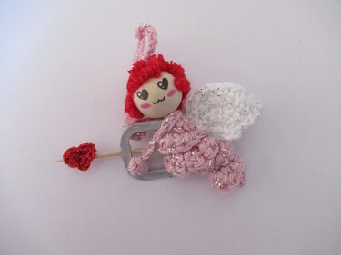 Gehäkeltes Amigurumi-Engelchen rosa mit weißen Flügeln und rotem Herzpfeil