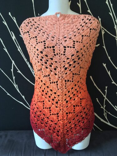 Gehäkeltes Dreieckstuch in Ombre-Farben von Lachsrosa zu Weinrot mit Lochmuster und Herzdetail auf einer Schneiderpuppe.