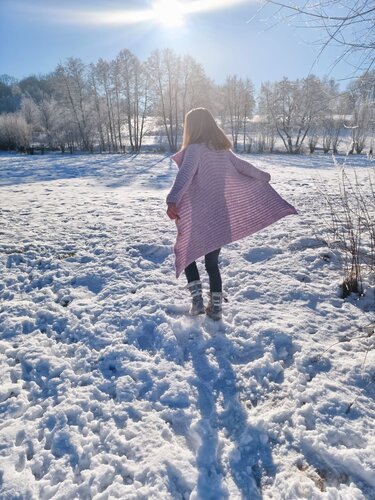 Person von hinten mit langer, offen gehäkelter rosa Jacke im Schnee
