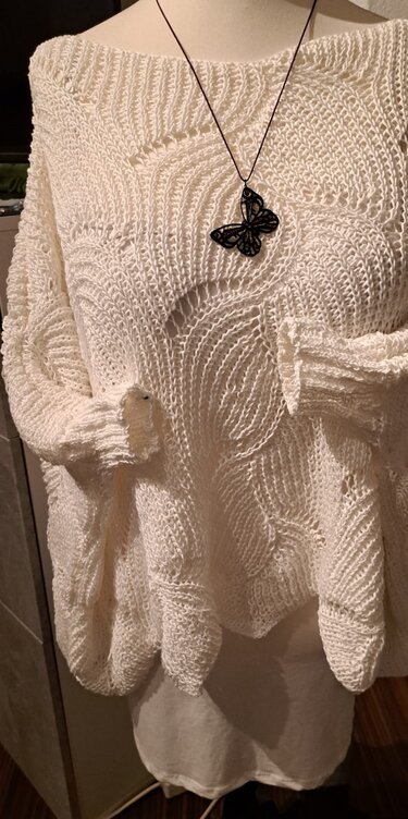 Cremefarbener, locker gestrickter Damenpullover mit Ajour‑Wellenmuster auf einer Schneiderbüste, ergänzt durch eine schwarze Schmetterlingskette.