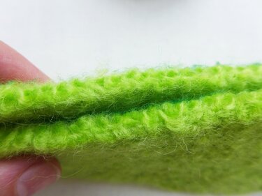 Zwei Lagen limettengrüner Strickfilz, an der Kante von Fingern gehalten