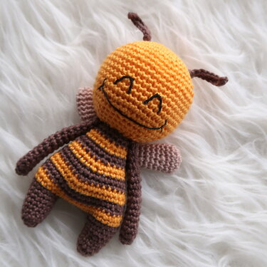 Gehäkelte Amigurumi-Biene mit gesticktem Lächeln auf weißem, flauschigem Untergrund