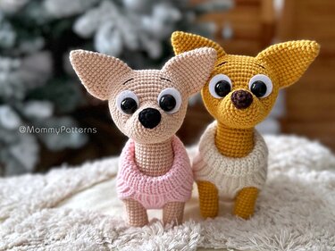 Zwei gehäkelte Amigurumi‑Hunde, einer rosa mit rosa Pullover, einer senfgelb mit cremefarbenem Pullover, auf flauschigem Untergrund