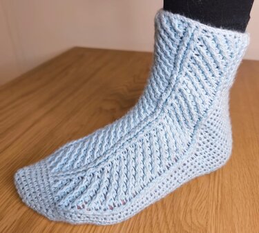 Detailansicht einer hellblauen gehäkelten Socke mit diagonalen Rippen und wabenartiger Fersenstruktur