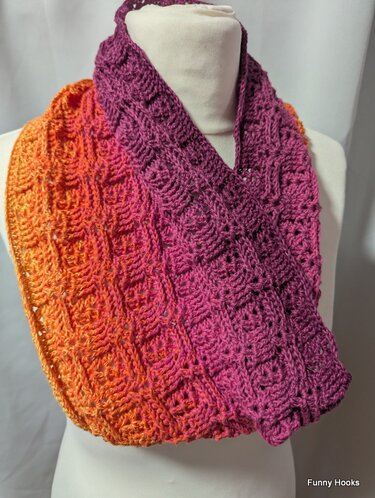 Gehäkelter Loop‑Schal in Orange‑ und Violetttönen auf einer Büste, strukturiertes Häkelmuster sichtbar.