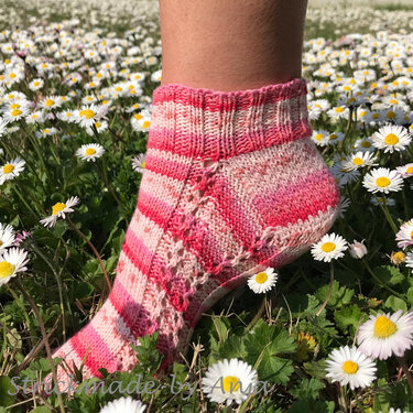 Rosa-weiß gestreifte Knöchelsocke mit Ajour-Lochmuster an einem Fuß auf Wiese mit Gänseblümchen