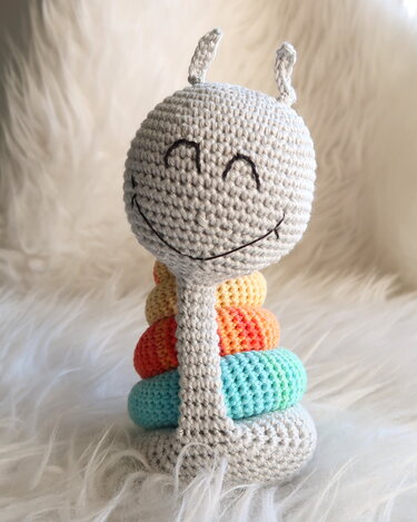 Gehäkelte Amigurumi‑Schnecke mit grauem Kopf und bunten Ringen