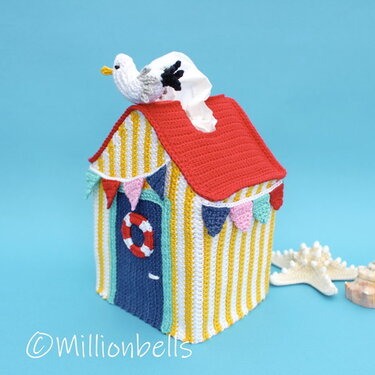 Crochet beach hut tissue box cover with red roof, yellow-and-white stripes, blue door, and seagull tissue dispenser.