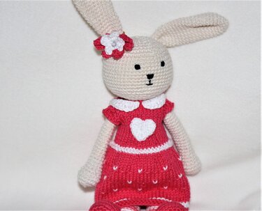 Gehäkelter Amigurumi-Hase mit himbeerrotem Kleid, weißem Herz und Blume am Ohr