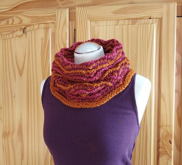 Gestrickter Loop‑Schal mit pink‑orangem Streifenmuster auf einer Schneiderpuppe