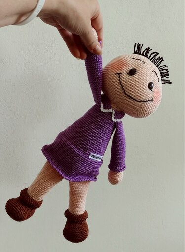 Nahaufnahme: handgehäkelte Amigurumi-Puppe mit lila Kleid, weißem Kragen und braunen Stiefeln.