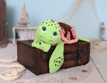 Lime-green crocheted sea turtle amigurumi with brown and pink shell on a trunk