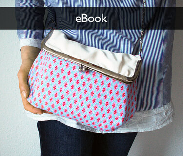 Retro-Handtasche mit Metallrahmen und rosa-blauem Blumenmuster vor gestreiftem Hemd