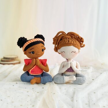 Two crocheted amigurumi dolls seated cross-legged in meditation, hands pressed together.