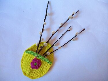 Gehäkeltes gelbes Osterkörbchen mit grüner Borte, pinker Blume und Weidenkätzchenzweigen