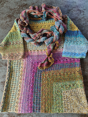 Bunt gehäkelte Tunika mit passendem Schal auf dunklem Untergrund ausgebreitet.