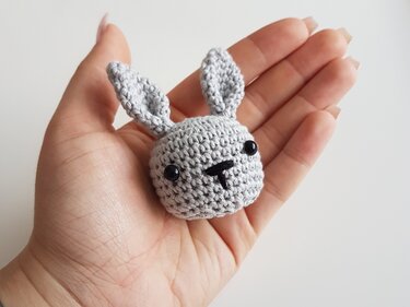 Hand hält kleinen gehäkelten grauen Amigurumi-Hasenkopf mit Ohren