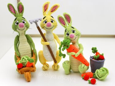 Three crocheted amigurumi rabbits, two green and one yellow, with miniature garden tools and crocheted vegetables
