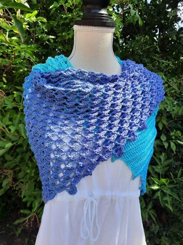 Asymmetrical turquoise-to-blue crochet shawl with lace mesh and textured panel draped on a dress form