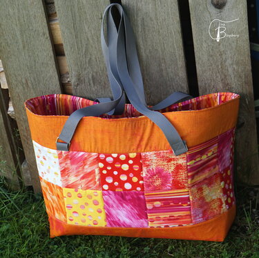 Orangefarbener Patchwork-Shopper mit bunten Quadraten und grauen Trägern, an einer Holzlattenwand gelehnt