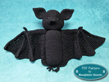 Schwarze gehäkelte Fledermaus Amigurumi mit ausgebreiteten Flügeln auf türkisfarbenem Untergrund