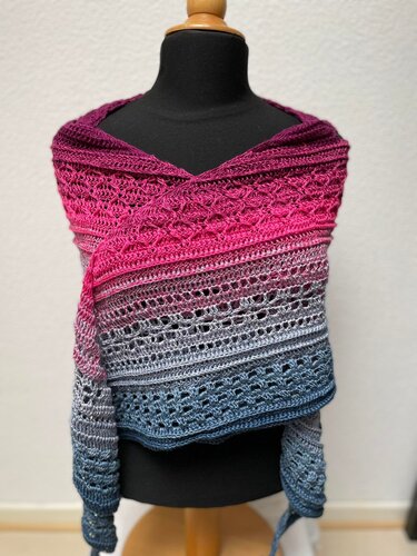 Gehäkeltes Halbrundtuch auf einer Schneiderpuppe mit Farbverlauf von Magenta zu Grau und Blau und verschiedenen Häkelmustern.