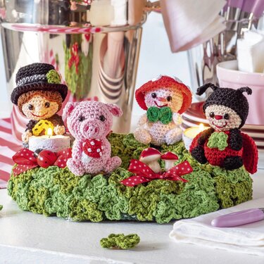 Gehäkelte Amigurumi-Glücksfiguren auf grünem Häkelkranz mit Schleifen und Teelicht