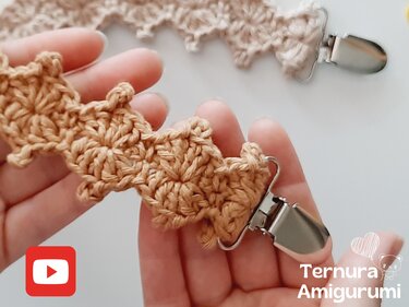 Hand holding light brown crocheted baby clip with metal clasp and scalloped stitch pattern.