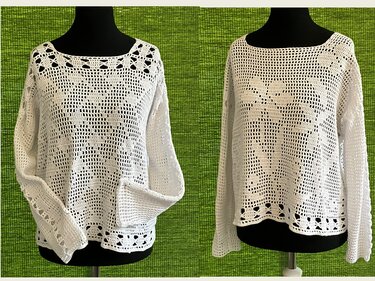 Weißes gehäkeltes Damenshirt mit Filetmuster auf schwarzer Schneiderpuppe vor grünem Hintergrund
