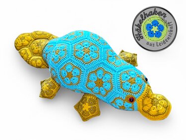 Blue and yellow crocheted platypus made from African flower granny motifs on a white background.