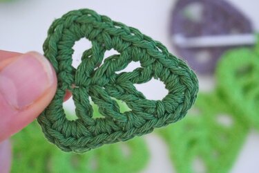 Hand holding dark green crocheted leaf-shaped motif with openwork stitches.
