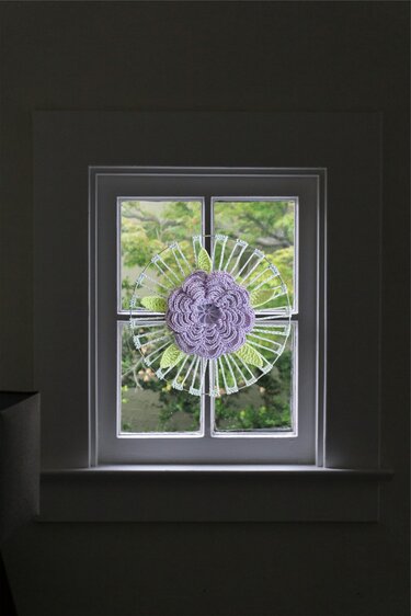 Gehäkelte lila Blume mit grünen Blättern als Fenster- oder Wanddekoration