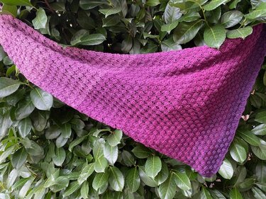 Gehäkeltes Dreieckstuch in Lila und Pink mit strukturiertem Muster auf grünen Blättern