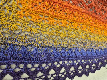Detailaufnahme des Häkelmusters und Farbverlaufs eines Dreieckstuchs in Orange, Gelb, Blau und Lila