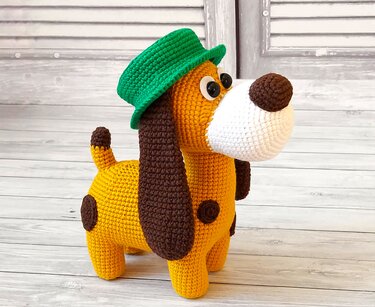 Gehäkelter Amigurumi-Hund in Gelb-Orange mit braunen Ohren, weißer Schnauze und grünem Hut