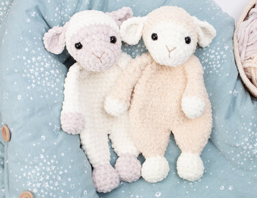 Two neutral crocheted lamb loveys on a pale blue star-patterned baby cushion