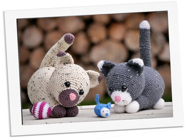 Zwei Amigurumi-Katzen mit gestreiftem Ball und kleiner blauer Spielzeugmaus