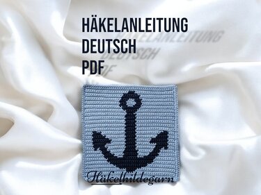 Gehäkeltes hellblaues Quadrat mit dunkelblauem Anker als Pixelmuster auf weißem Stoff