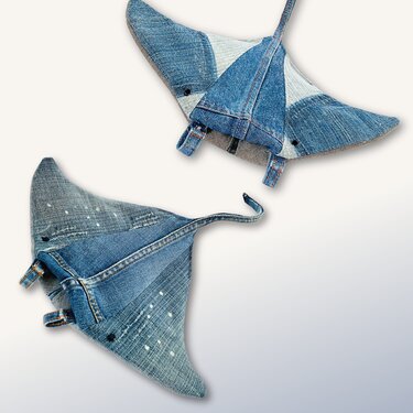 Two manta ray-shaped denim potholders in blue tones, one paint-splattered and one patchwork, on a light background.