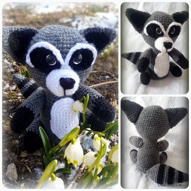 Gehäkelter Amigurumi-Waschbär mit schwarzer Augenmaske und geringeltem Schwanz zwischen Schneeglöckchen