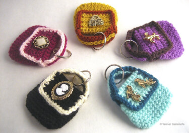 Fünf gehäkelte Mini-Täschchen als Schlüsselanhänger in verschiedenen Farben mit Metallringen und Zierbroschen