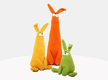 Three crocheted amigurumi rabbits in orange, yellow and green with long ears on a white surface
