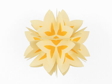 Gelbe und orange Papierdekoration in Form einer stilisierten Blume vor weißem Hintergrund