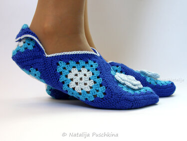 blaue gehäkelte Ballerina-Hausschuhe mit Granny-Squares und weißer Blüte, getragen an Füßen