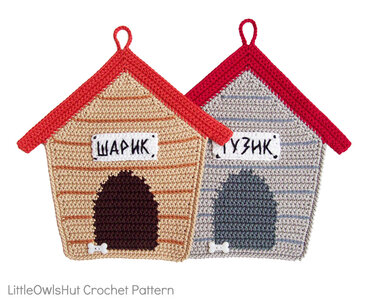Two crocheted doghouse-shaped potholders, beige and gray, with red roofs, dark entrances, white bone buttons and hanging loops.